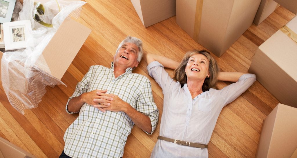 Man and woman lay happily on hardwood floor next to moving boxes.